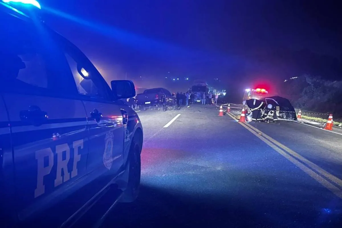 Imagem mostra um acidente na BR-476. Tem um carro da PRF e uma iluminação azul por causa do giroflex da viatura. Ao fundo, um carro destruído.