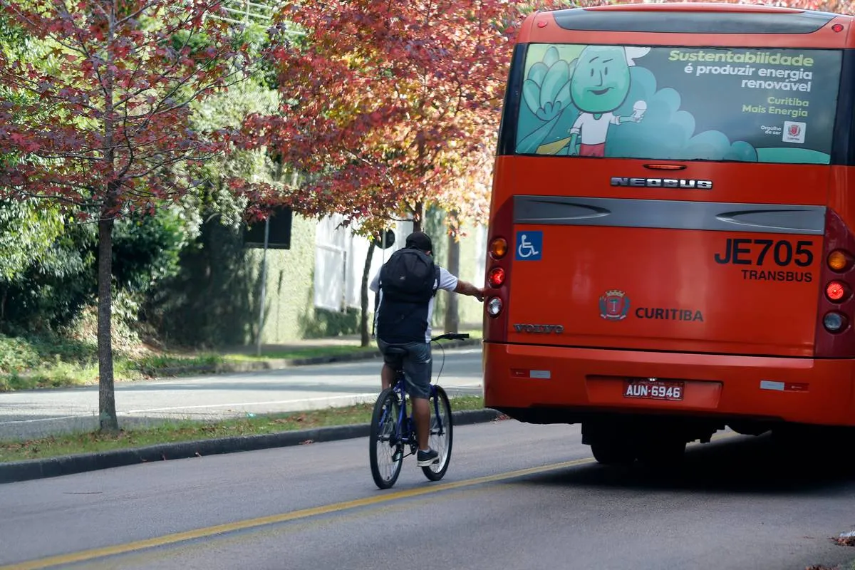 Imagem mostra uma pessoa em uma bicicleta pegando rabeira em um ônibus.