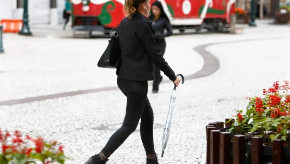 Imagem mostra uma mulher andando com um guarda-chuva na rua XV, em Curitiba.