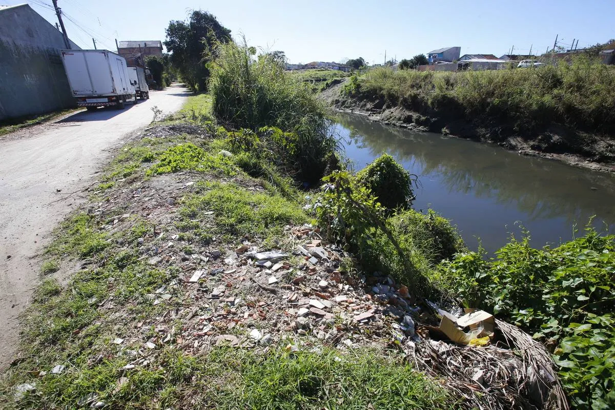 Imagem mostra muito lixo na beira de um rio de Curitiba