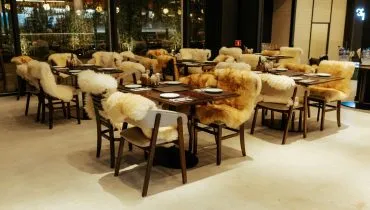 Foto mostra salão do restaurante, com mesas e cadeiras com pelegos de carneiro