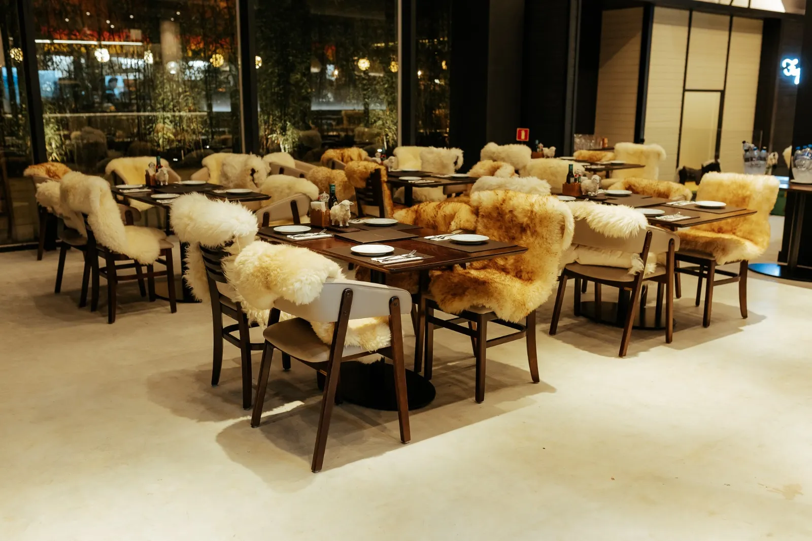 Foto mostra salão do restaurante, com mesas e cadeiras com pelegos de carneiro