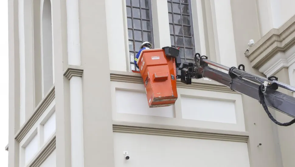 Operário içado em guindaste instala iluminação em janela da igreja