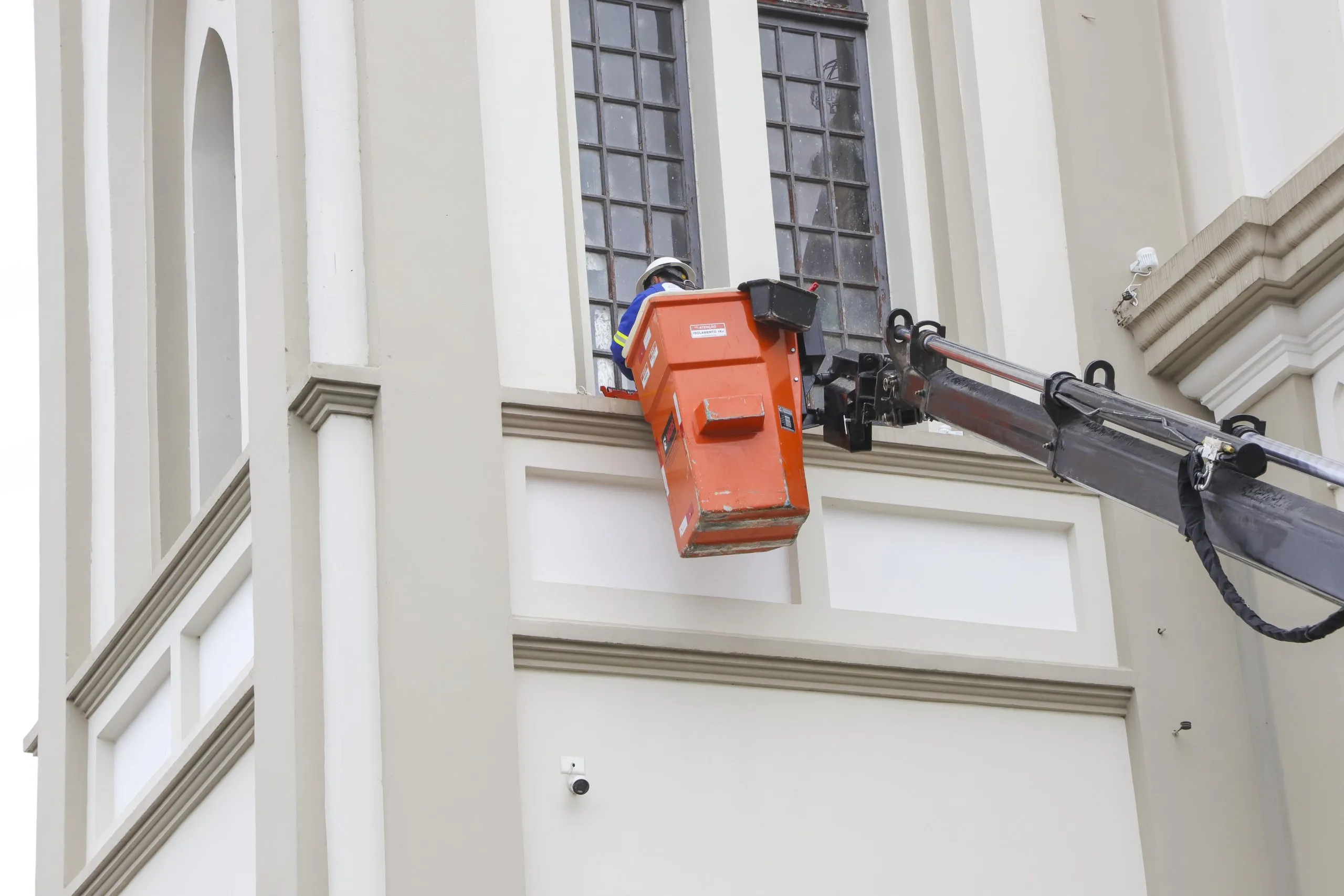 Operário içado em guindaste instala iluminação em janela da igreja