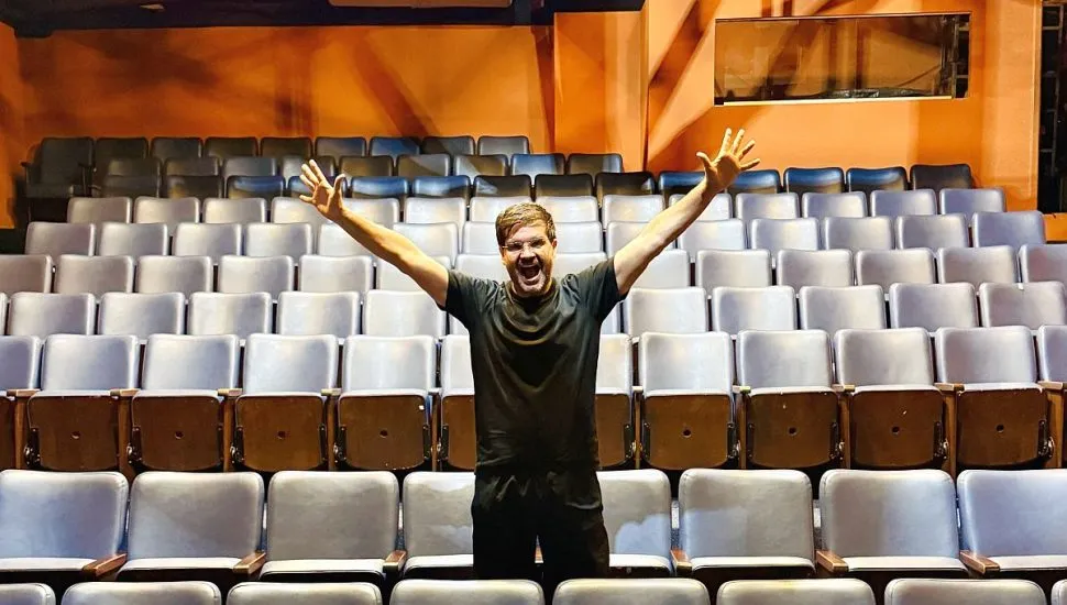 Imagem mostra Ilan, o Moço do Te Amo, no meio do auditório do teatro Barracão Encena.