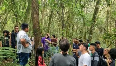 Imagem mostra várias pessoas ouvindo um guia falar no meio da floresta