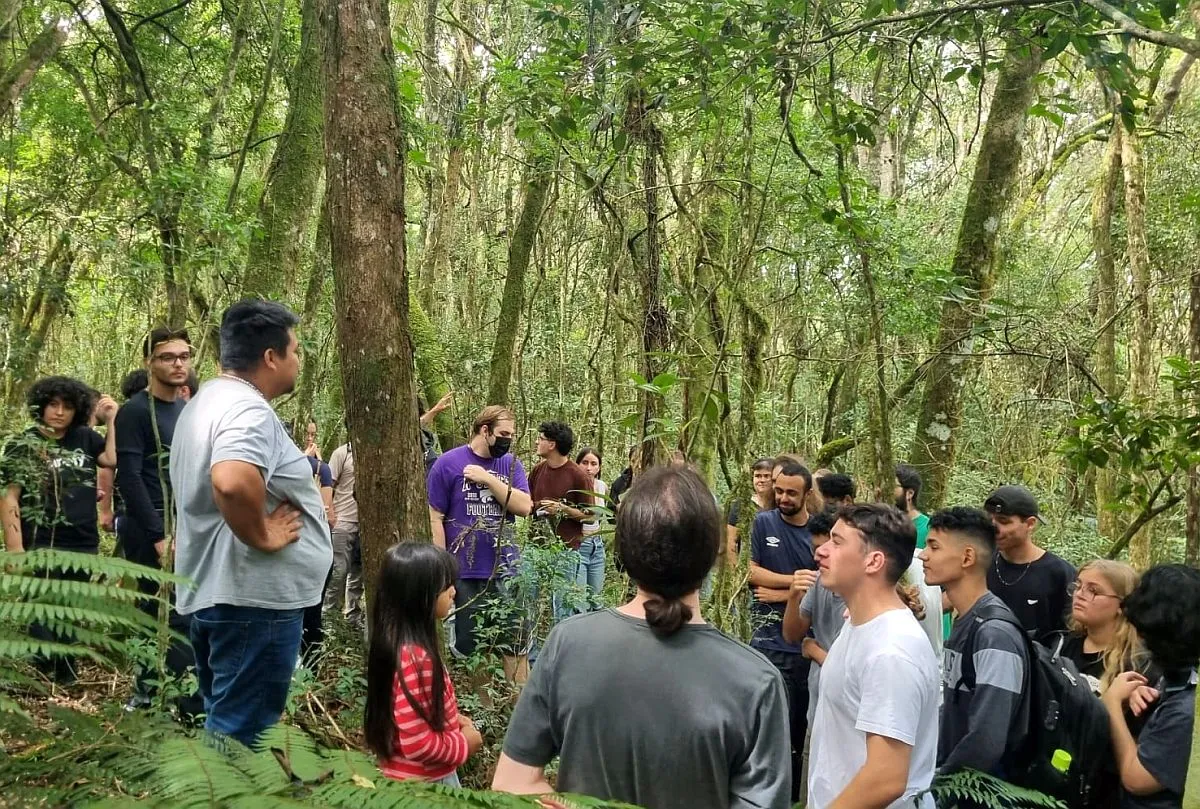 Imagem mostra várias pessoas ouvindo um guia falar no meio da floresta