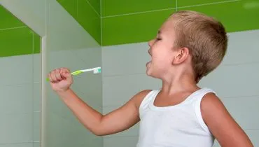 Menino segura uma escova de tente, em frente a um espelho, simulando usar um microfone