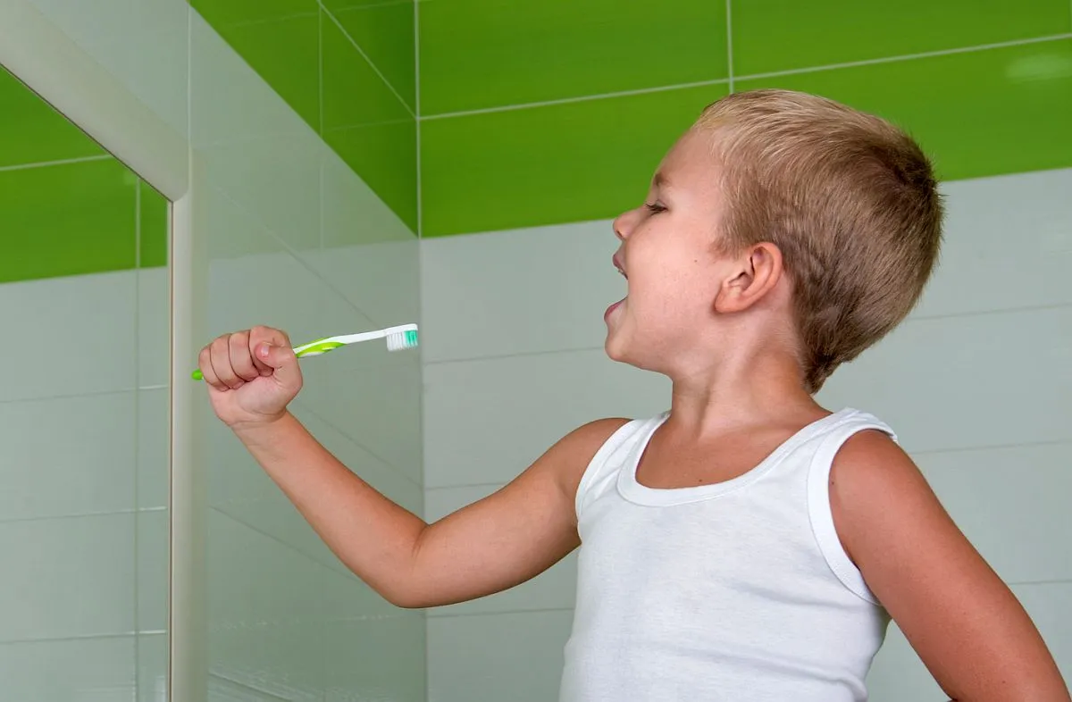 Menino segura uma escova de tente, em frente a um espelho, simulando usar um microfone