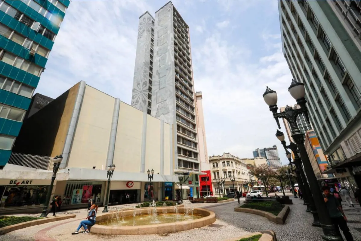 Imagem mostra um prédio de Curitiba com céu azul com nuvens.