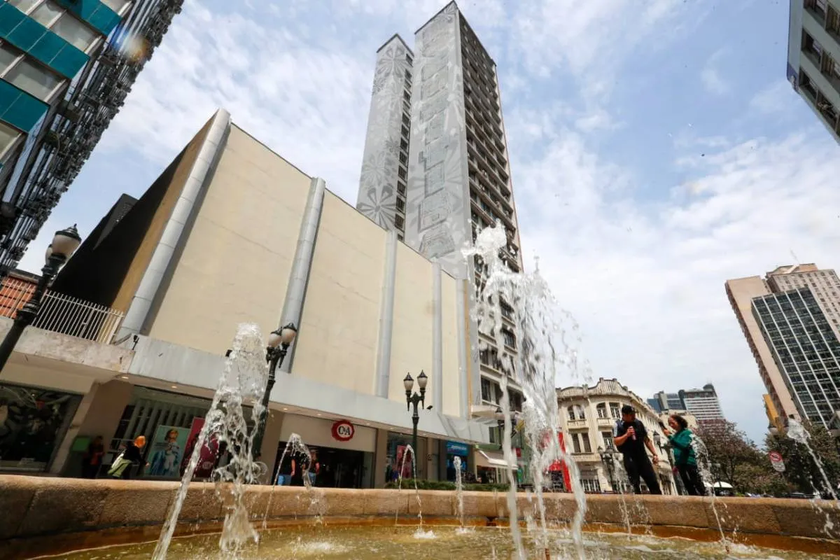 Imagem mostra um prédio de Curitiba com céu azul com nuvens.