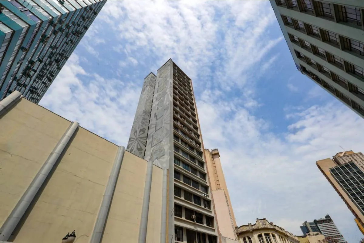 Imagem mostra um prédio de Curitiba com céu azul com nuvens.