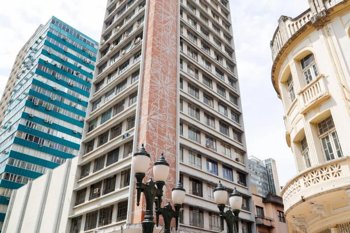 Imagem mostra um prédio de Curitiba com céu azul com nuvens.