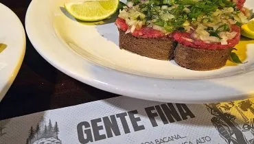Imagem mostra uma carnde de onça servida sobre um papel com o nome do bar Gente Fina