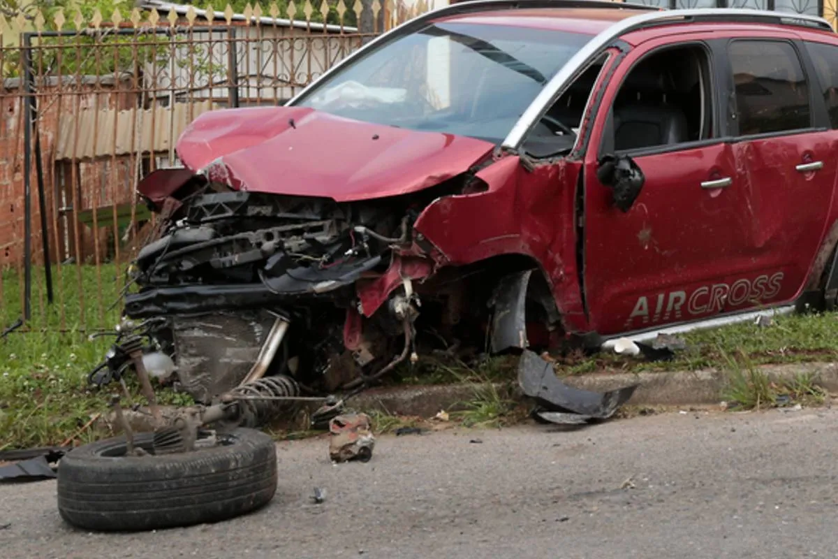 Imagem mostra um carro vermelho acidentado.