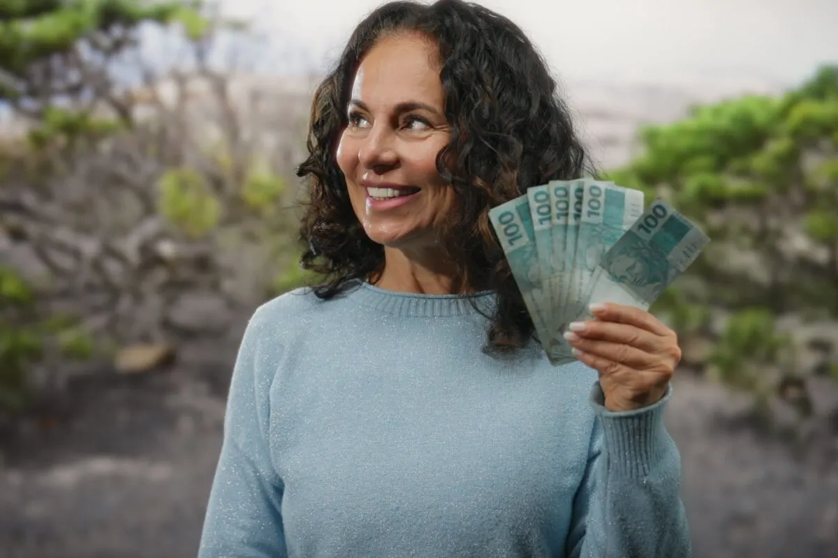 Imagem mostra uma mulher vestida com uma blusa azul segurando notas de real.