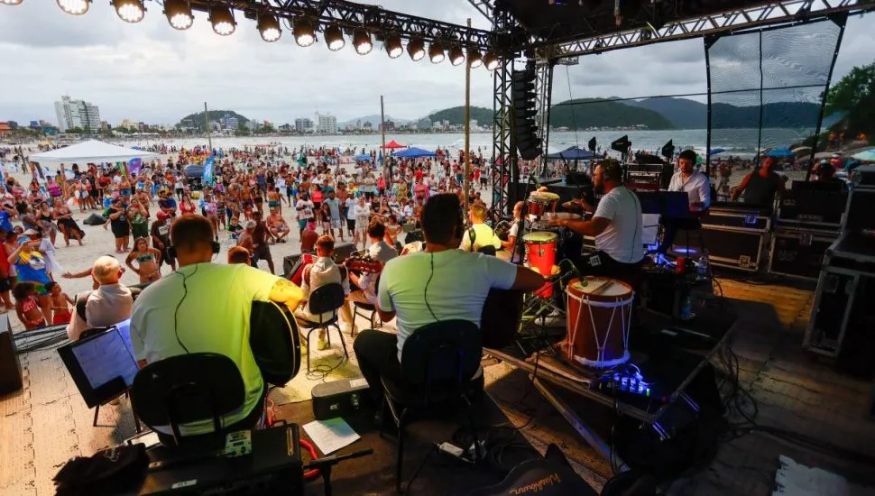 Imagem mostra um show em uma praia com vista do palco para o público.