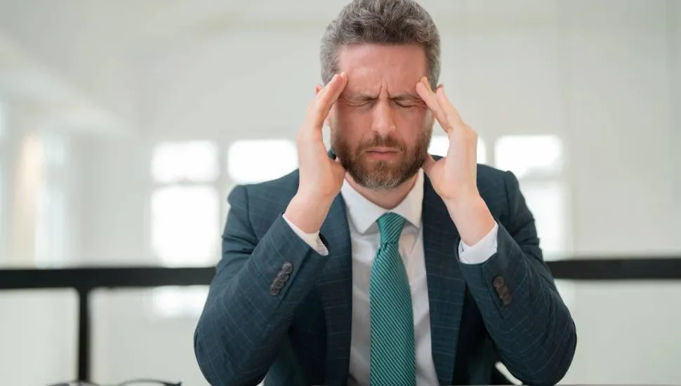 Imagem mostra um homem de terno e gravata com dor de cabeça.