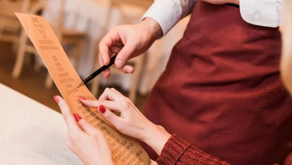 Imagem mostra uma pessoa pedindo um prato em um restaurante, olhando o menu