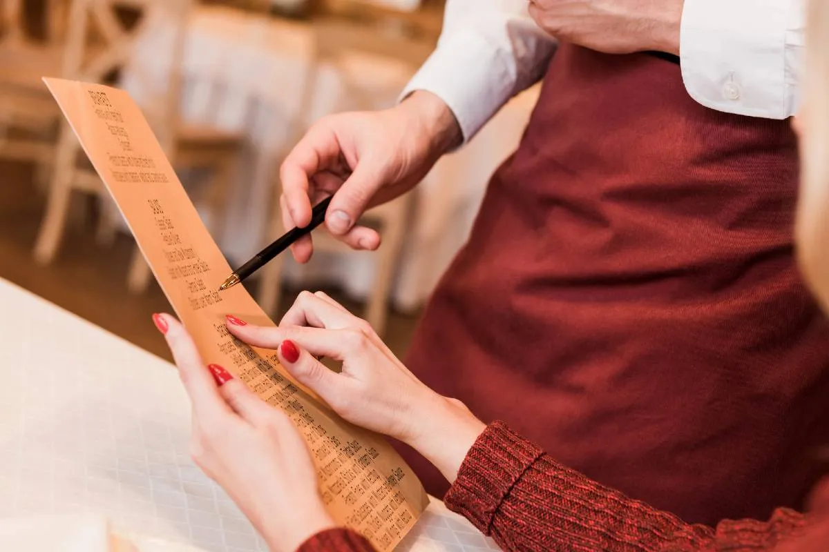 Imagem mostra uma pessoa pedindo um prato em um restaurante, olhando o menu