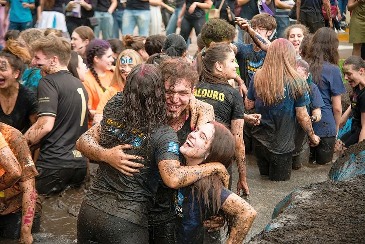 Dezenas de pessoas se abraçam e comemoram dentro de um piscinão de lama