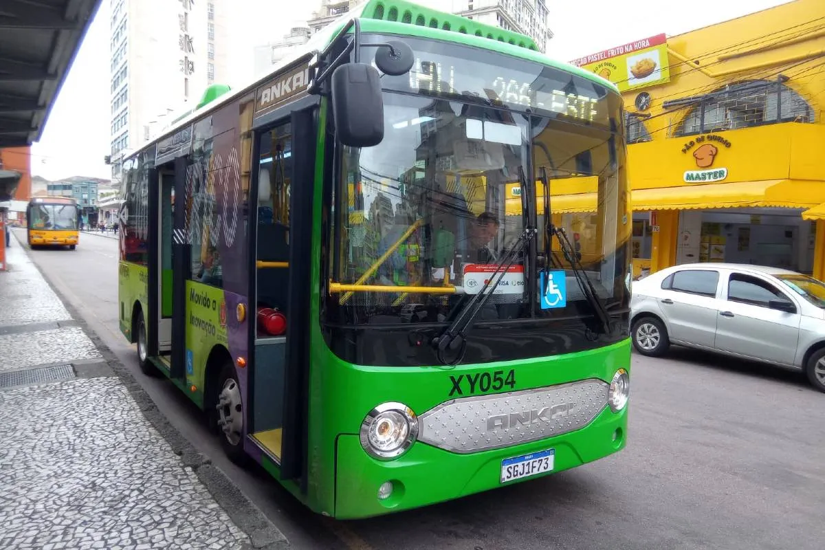 Imagem mostra um micro ônibus elétrico  de cor verde flagrado circulando pelas ruas de Curitiba em uma linha de transporte coletivo.