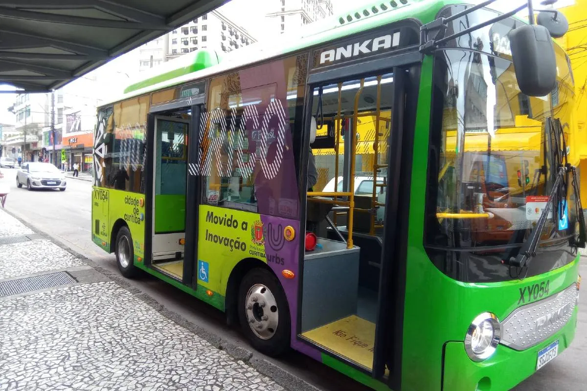 Imagem mostra um micro ônibus elétrico  de cor verde flagrado circulando pelas ruas de Curitiba em uma linha de transporte coletivo.