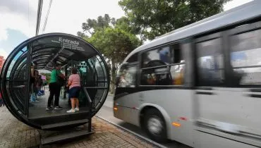 Imagem mostra um ligeirinho prateado chegando a uma estação-tubo de Curitiba.