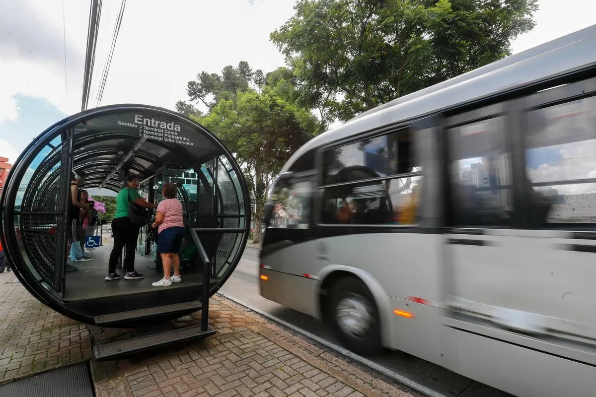 Imagem mostra um ligeirinho prateado chegando a uma estação-tubo de Curitiba.