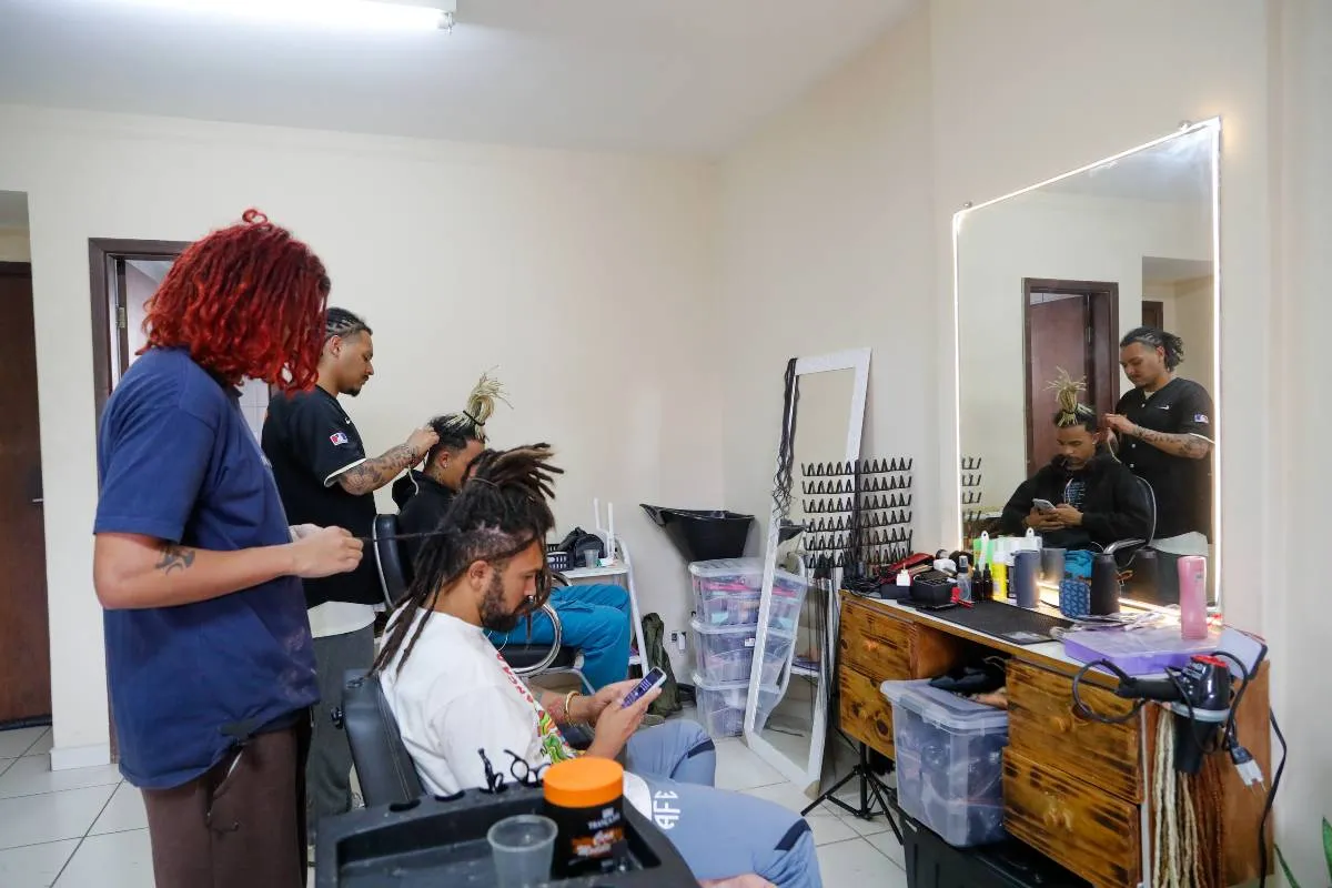 Imagem mostra um salão onde pessoas fazem dreadlocks no cabelo.