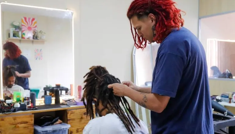 Imagem mostra uma pessoa fazendo dreadlocks em outra.