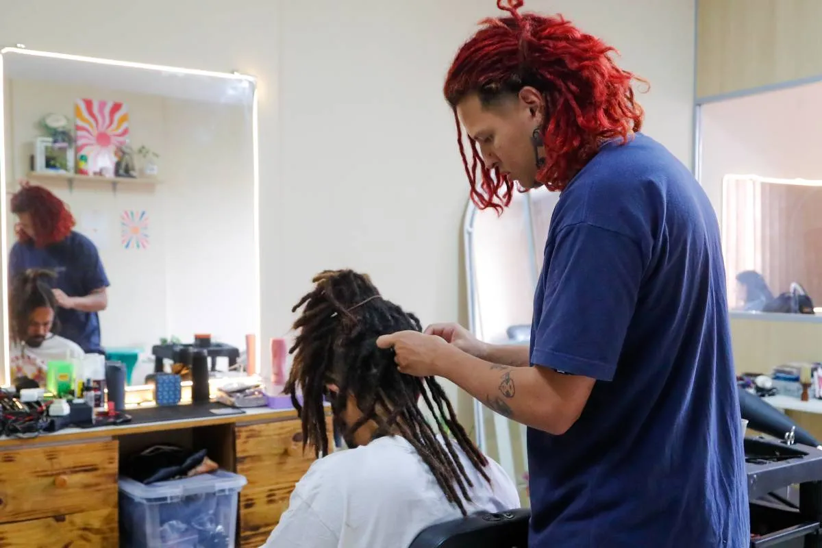 Imagem mostra uma pessoa fazendo dreadlocks em outra.