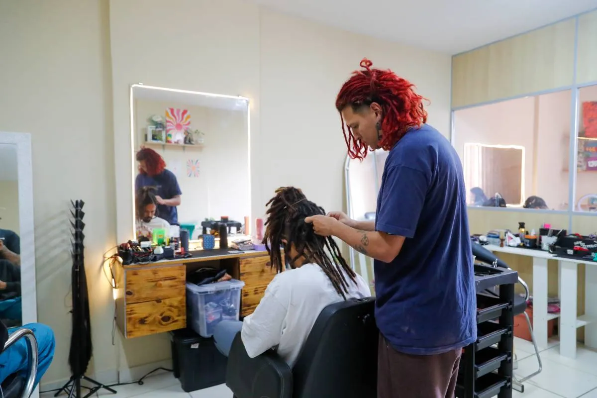 Imagem mostra uma pessoa fazendo dreadlocks em outra.