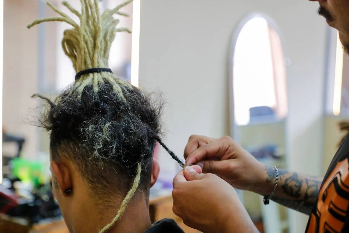 Imagem mostra uma pessoa fazendo dreadlocks em outra.