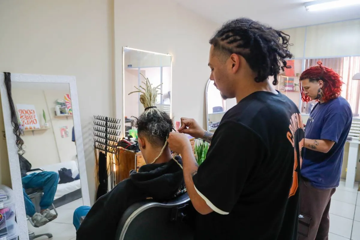 Imagem mostra uma pessoa fazendo dreadlocks em outra.