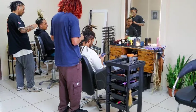 Imagem mostra um salão onde pessoas fazem dreadlocks no cabelo.