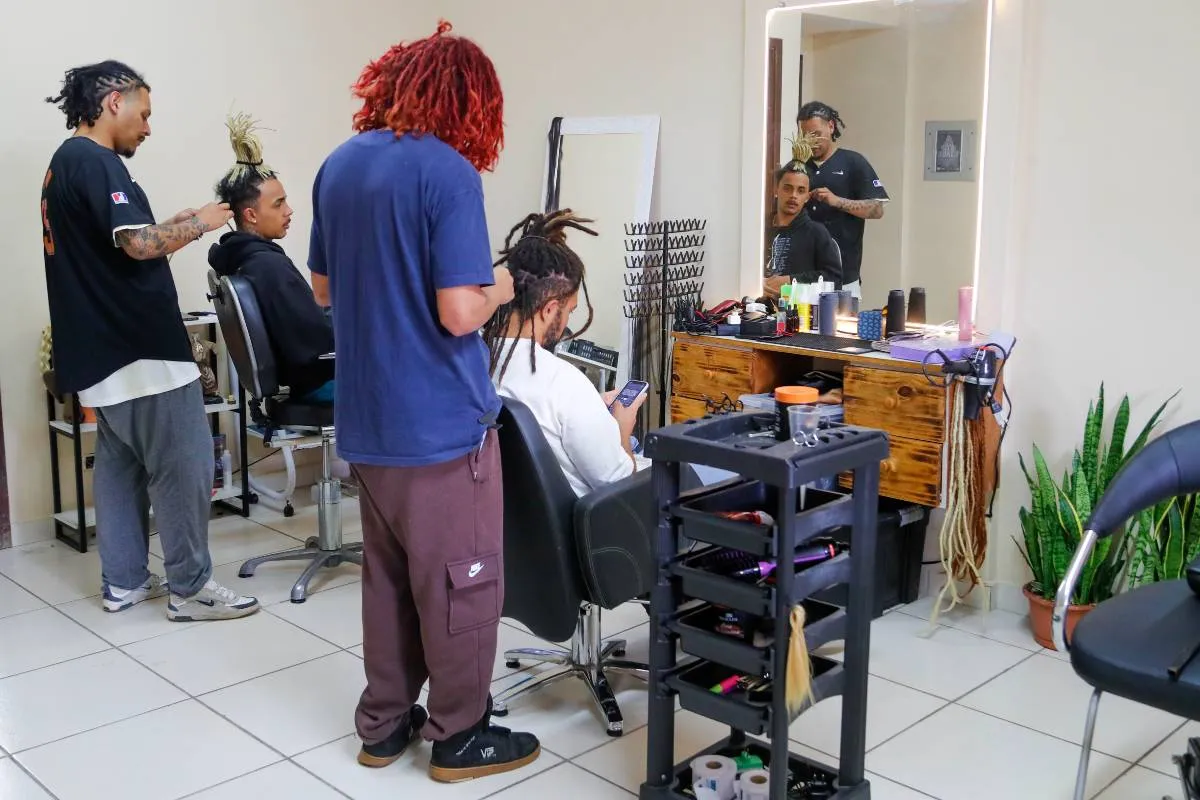 Imagem mostra um salão onde pessoas fazem dreadlocks no cabelo.