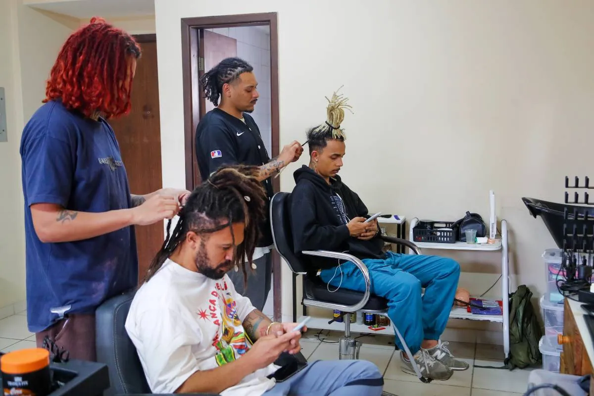 Imagem mostra um salão onde pessoas fazem dreadlocks no cabelo.