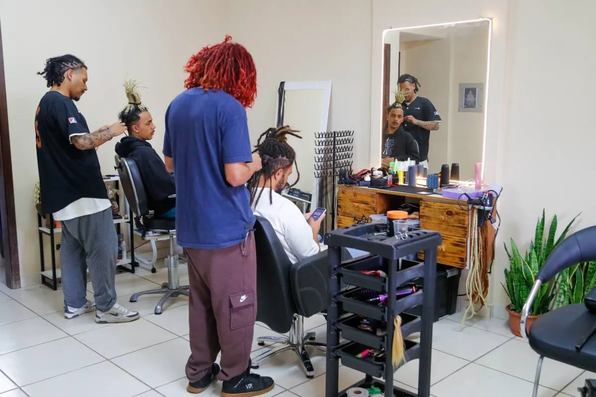 Imagem mostra um salão onde pessoas fazem dreadlocks no cabelo.