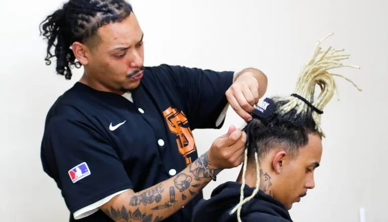 Imagem mostra uma pessoa fazendo dreadlocks em outra.