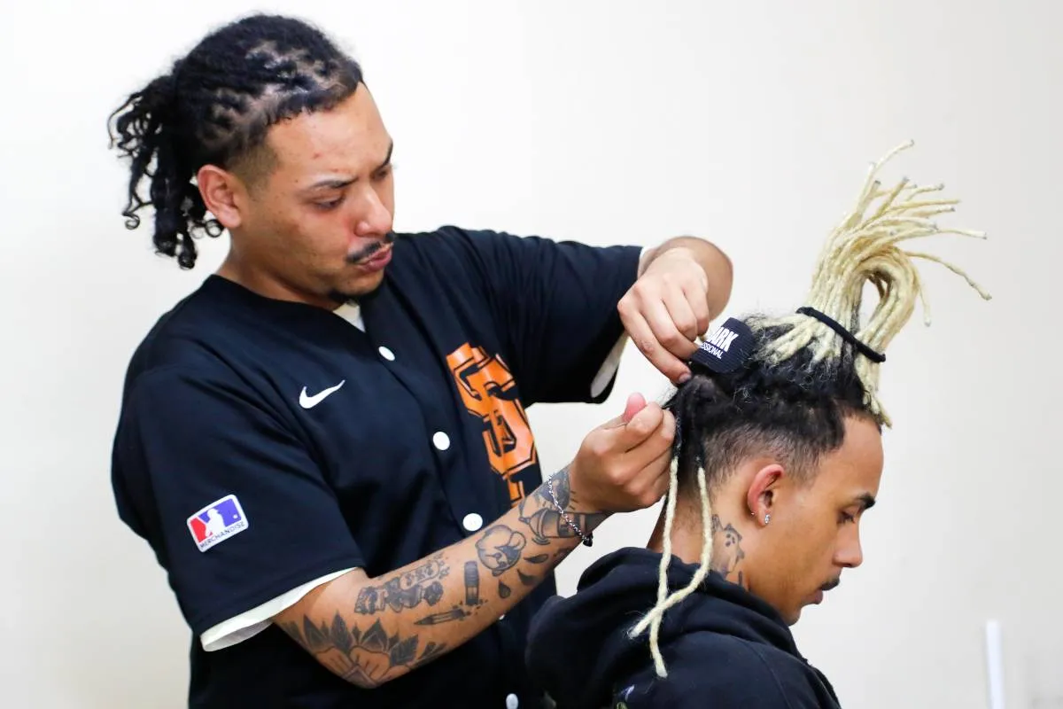 Imagem mostra uma pessoa fazendo dreadlocks em outra.