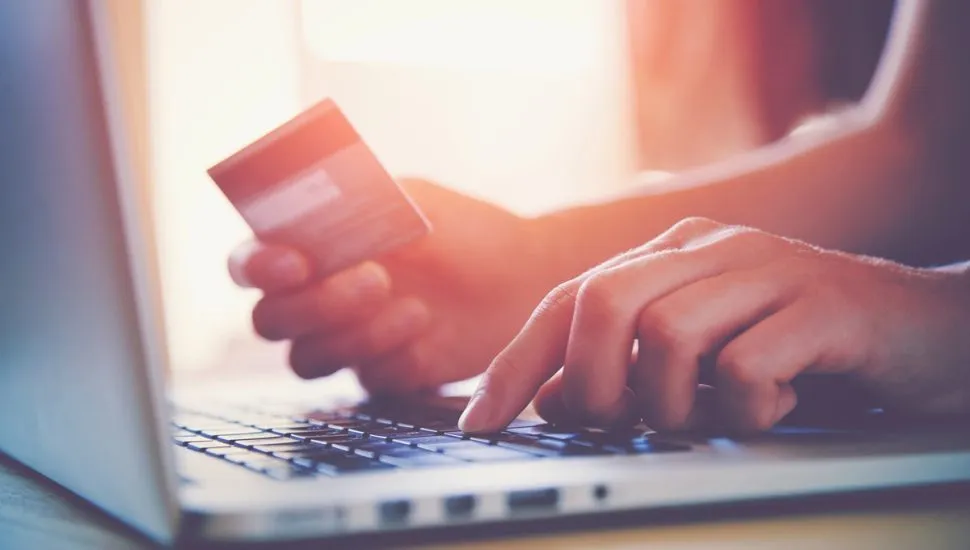 Imagem mostra mulher realizando compra online, com o cartão de crédito na mão