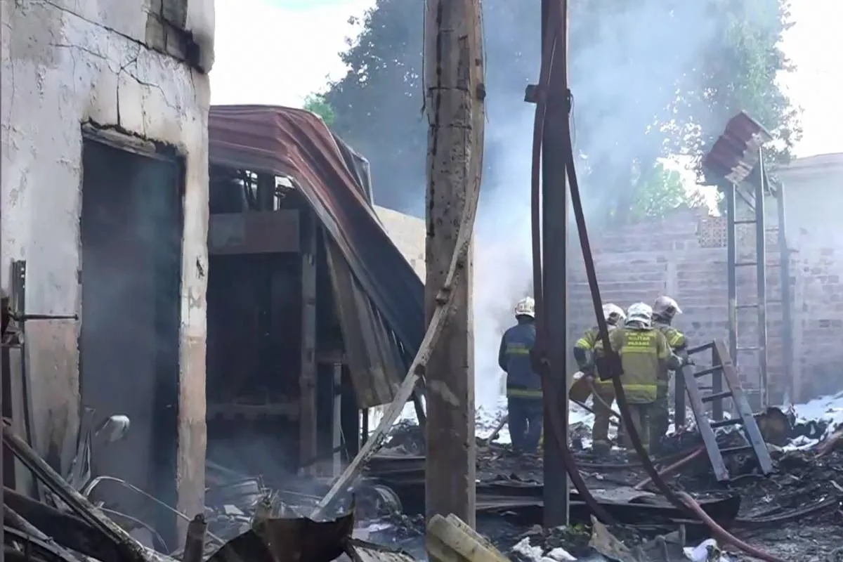 Imagem mostra bombeiros apagando o fogo em um incêndio em um barracão. Há muitas coisas queimadas.