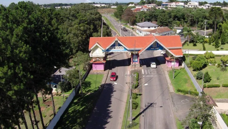 Imagem aérea mostra o portal de Araucária em um dia de sol. com árvores ao lado e carro passando na estrada.