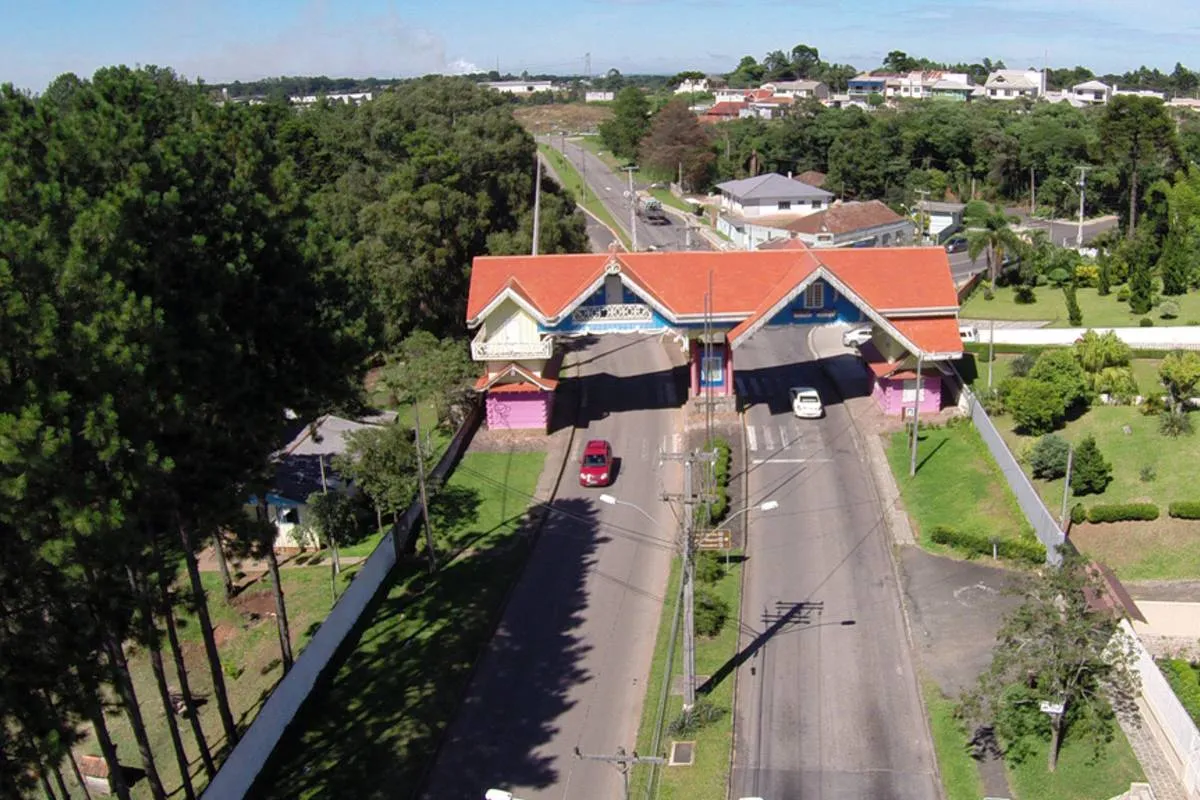 Imagem aérea mostra o portal de Araucária em um dia de sol. com árvores ao lado e carro passando na estrada.