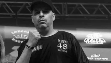 Imagem em preto e branco mostra um homem com camiseta, boné e um punho cerrado.