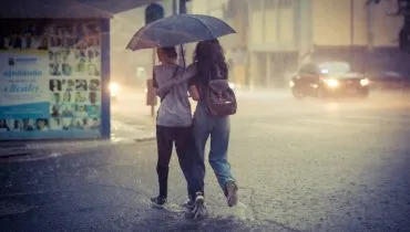 Chuva intensa em Curitiba. Imagem mostra uma mulher e um estudante atravessando uma rua correndo com um guarda chuva