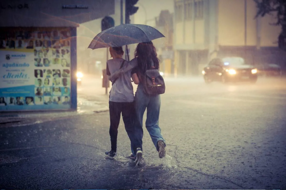 Chuva intensa em Curitiba. Imagem mostra uma mulher e um estudante atravessando uma rua correndo com um guarda chuva