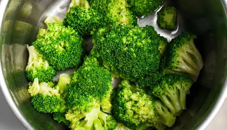 Imagem mostra um brócolis cozinhando na água.