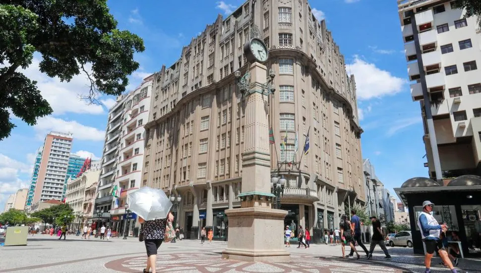 Imagem mostra um prédio em Curitiba, com céu azul e um grande relógio ao centro.